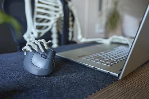 Skeleton hand resting on computer mouse beside open laptop on office desk 写真素材