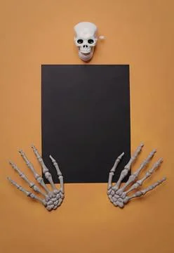 Skeleton hands holding black blank paper on orange background Stock Photos