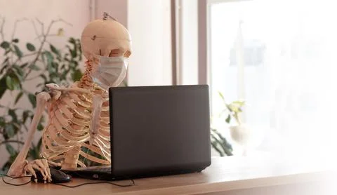 Skeleton in a medical mask using a computer in the office Stock Photos