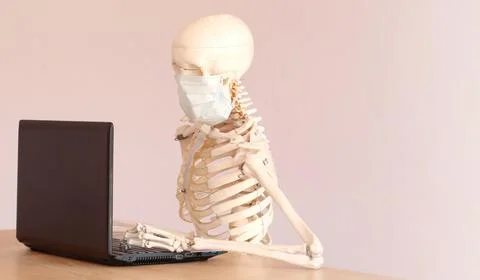 Skeleton in a medical mask using a computer in the office Stock Photos