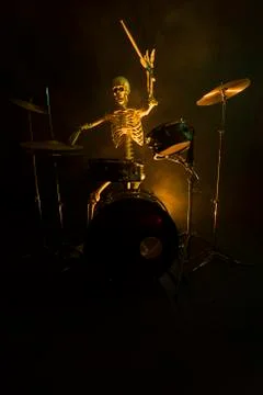 Skeleton playing a drum set in the dark lit by yellow light Stock Photos