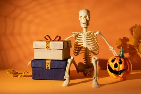 Skeleton with stacked gift boxes and jack o lantern on orange background fo.. Stock Photos