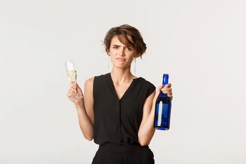 Skeptical and displeased young woman grimacing upset, holding bottle and glass Stock Photos