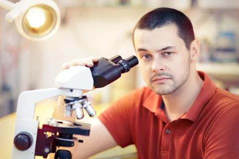 Skeptical Young Male Researcher with microscope Stock Photos