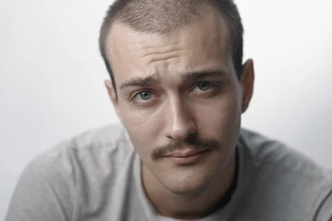 Skeptical young man with mustache looking at camera with doubtful expression 스톡 사진