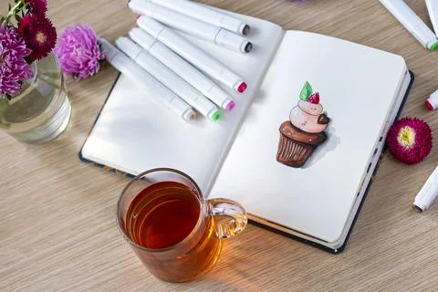 Sketching cupcake in a notebook. All placed on a wooden table with a transpar Stock Photos