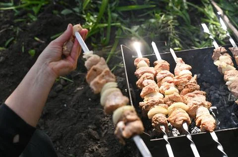 Skewer with raw chicken being threaded by hand over grill. Skewer held abov.. Fotos de archivo