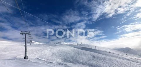 Ski slope, chair-lift on ski resort and blue sky with sunlight clouds Stock Photos