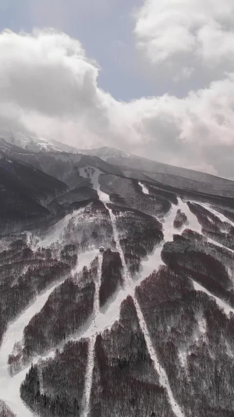 Ski trail vertical Aerial fly snowy mountain peaks with clouds, winter Aomori Stock Footage 331240664