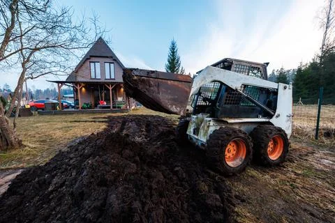 Skid steer earthmoving by A frame cabin with carport at dusk Stock Photos