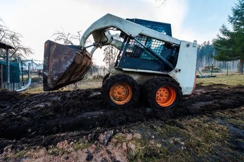 Skid Steer Loader Digging Muddy Trench Near Fencing and Trees Stock Photos