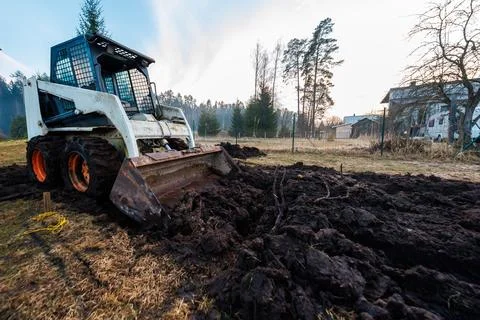 Skid Steer Loader Digs Muddy Soil at Dawn on Rural Property Fotos Stock