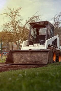 Skid Steer Loader on Dirt Patch with Grass and Leafless Trees 스톡 사진