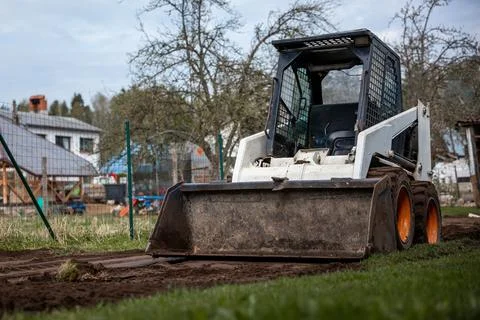Skid Steer Loader on Dirt Path Near Fenced Area and Houses Stock Photos