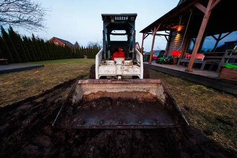 Skid Steer Loader Grading Soil at Suburban Patio at Dusk Stock Photos