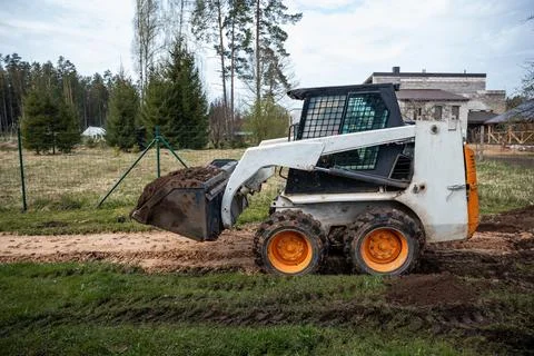 Skid Steer Loader Moving Soil on Dirt Path Near Evergreen Trees Stock Photos