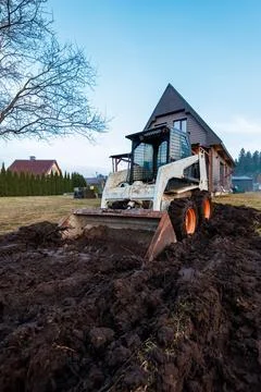 Skid Steer Loader in Mud Beside Steep Roofed A Frame Cottage Stock Photos