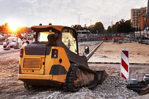 A skid steer loader stands at a construction site at sunset. Stock Photos
