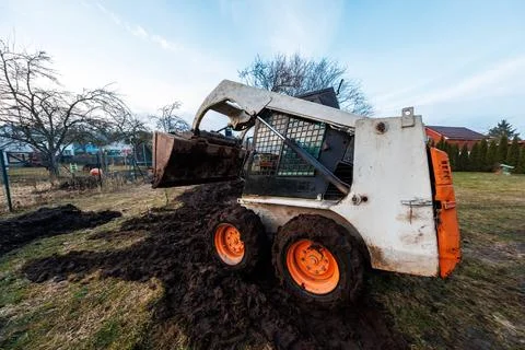Skid steer loader stuck in backyard mud pit with raised bucket Stock Photos