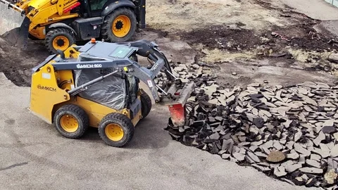 Skid steer loader using hydraulic breaker to demolish asphalt road. Stock Footage 328969084