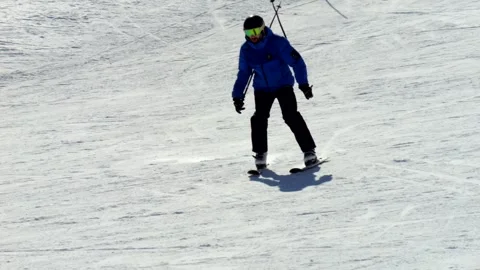 Skier in a blue jacket making a sharp turn on a snowy slope in 4K slow motion Vidéo 303092822