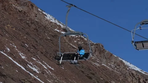Skier in a blue jacket rides a ski lift in the mountains on a sunny day Vidéo 303093075
