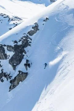 Skier drops into steep slope below granite cliff in the backcountry of Alaska Stock Photos