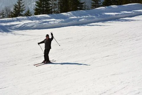 A skier is going down a steep ski track and waving his hand with a pole Stock Photos