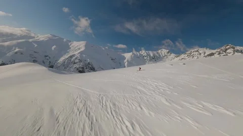 Skier in a red jacket and a black backpack descends along a snow-white ridge. In Stock Footage 275207324