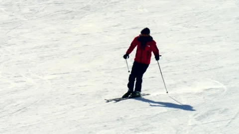 Skier in a red jacket rapidly descends a snowy mountain slope on a sunny day Vidéo 303093078
