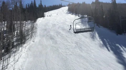 Skiers going down a slope on a sunny day shot from chairlift in Park City Utah Stock Footage 61863523