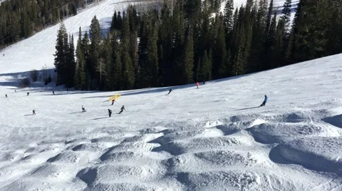 Skiers going down a slope on a sunny day shot from chairlift over bumps in Park Stock Footage 61863549