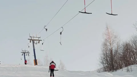 Skiers use a T-bar lift to climb a slope or hill on a sunny day at a ski resort Stock Footage 165116653