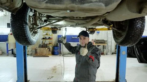 Skilled auto technician checking underside of raised vehicle, flashlight in hand Stock Photos