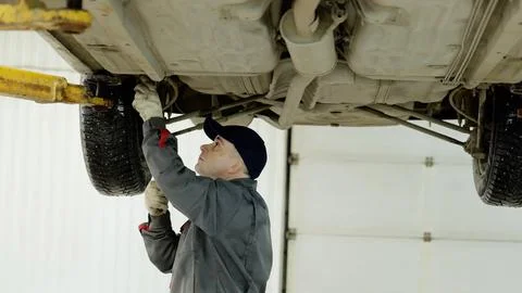 Skilled auto technician checking vehicle undercarriage, wearing protective gear Stock Photos