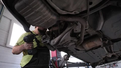 Skilled automotive technician working under a car in a garage, using a power 库存影片 333991035