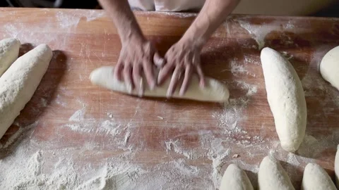 A skilled baker's hands expertly mold dough into a loaf shape on a rustic w.. Stock Footage 285176331