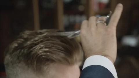 A skilled barber gently cutting through man's hair with scissors Video stock 117704771