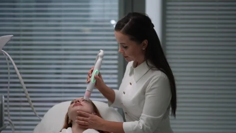 Skilled beautician using specialized device for mesotherapy on woman face in Stock Footage 310624167