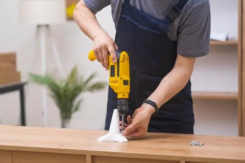 Skilled carpenter in blue overalls, using yellow electrical drill screwdriver Stock Photos