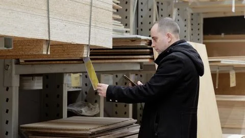 Skilled carpenter comparing lumber prices on smartphone, holding particle board Foto stock