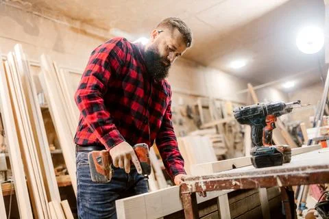 Skilled carpenter working in a workshop using a power drill to build wooden Stock Photos