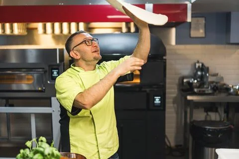 Skilled chef preparing dough for pizza rolling with hands and throwing up Stock Photos
