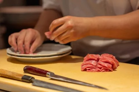 Skilled chef preparing thinly sliced meat on wooden cutting board Stock Photos
