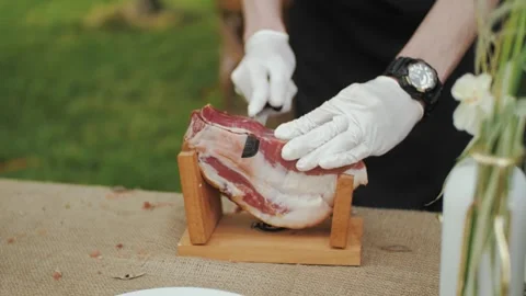 A skilled chef in white gloves cuts and prepares cured meat outdoors Stock Footage 308862556