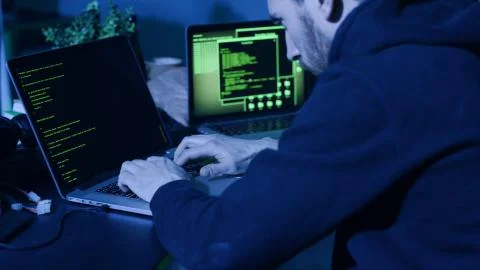 Skilled computer hacker typing code on laptop trying to steal critical Stock Photos