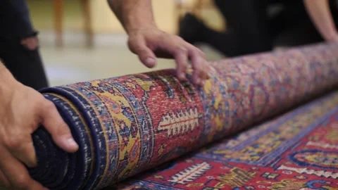Skilled conservators carefully roll an ornate antique carpet, showcasing Stock Footage 280261376