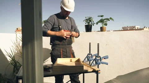 Skilled construction worker building wooden shelving unit on terrace as par.. Stock Footage 336026626