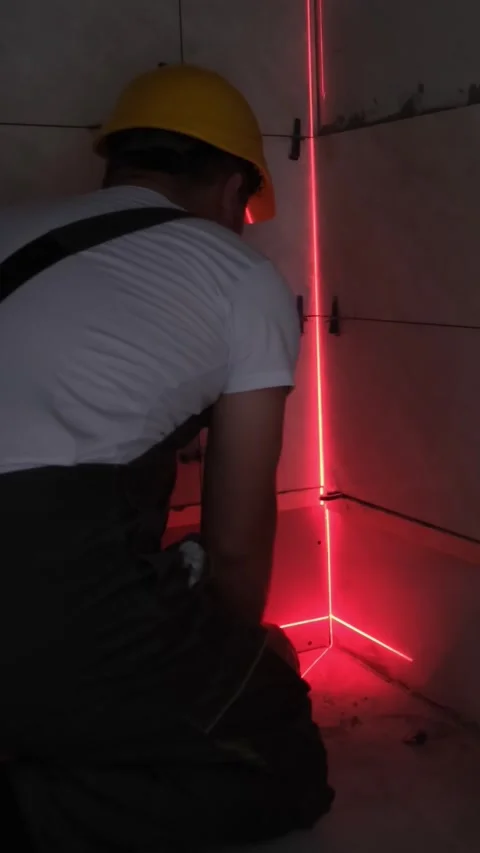 A skilled construction worker uses a laser level for precise tiling in a complex Video stock 312842050