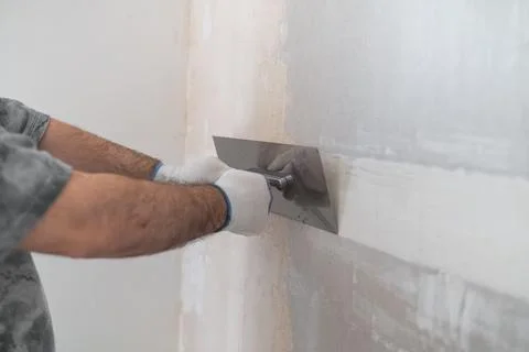 Skilled contractor applying finishing compound with stainless steel trowel on Stock Photos